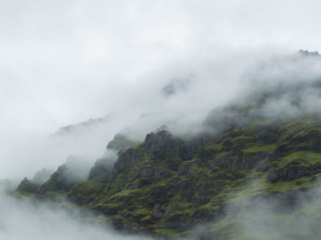 Clouds cling to a rough moss-covered small mountain